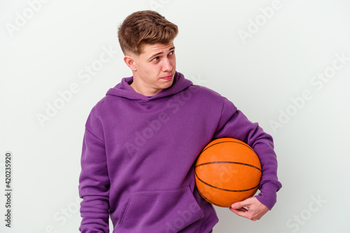 Young caucasian man playing basketball isolated background confused, feels doubtful and unsure.