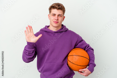 Young caucasian man playing basketball isolated background smiling cheerful showing number five with fingers.