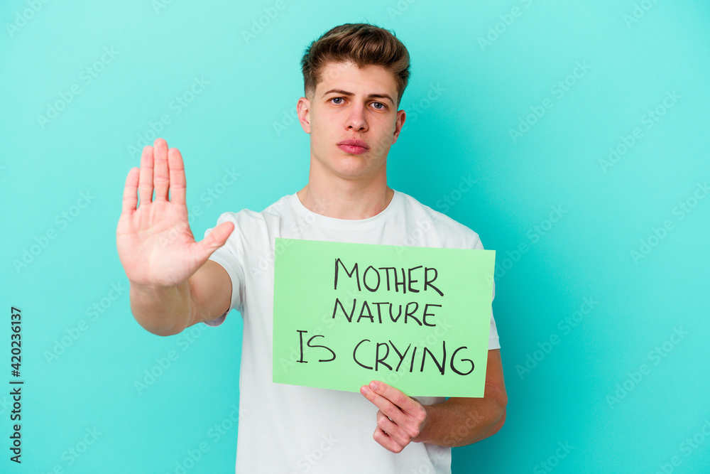 Young caucasian man holding a Mother Nature is crying placard isolated on blue background Young caucasian man holding a Mother Nature is crying placard isolated on blue background