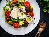 Fresh Greek salad - feta cheese, tomatoes, cucumber, lettuce, black olives and onion on wooden table
