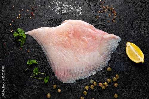 Fresh Ray wings fish with herbs on rustic black background