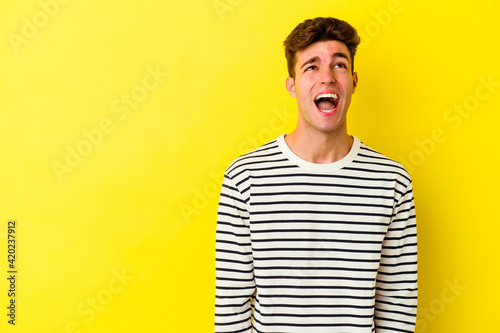 Young caucasian man isolated on yellow background shouting very angry, rage concept, frustrated.