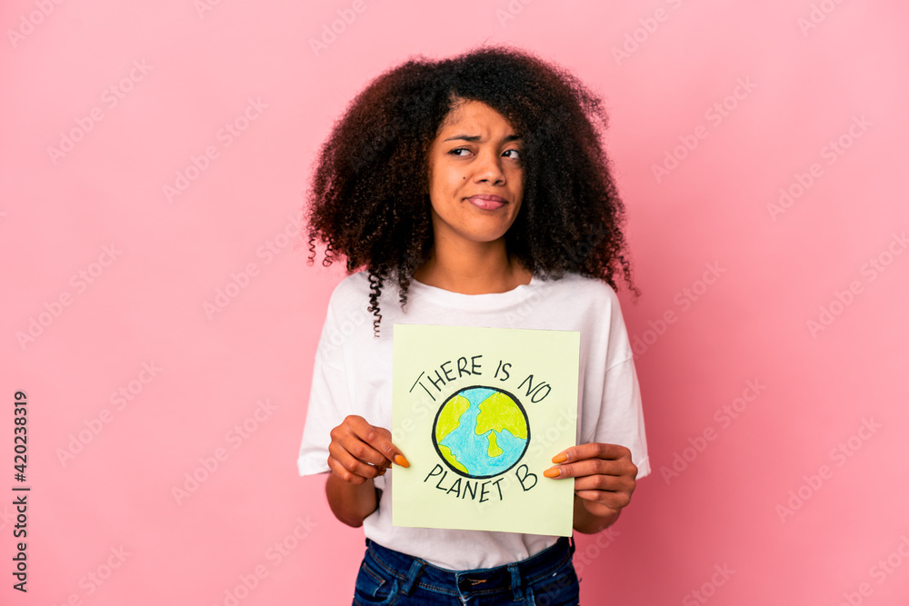 Young african american curly woman holding a planet message on a placard confused, feels doubtful and unsure. Young african american curly woman holding a planet message on a placard confused, feels doubtful and unsure.