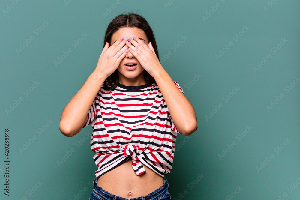 Young Indian woman isolated on blue background afraid covering eyes with hands.
