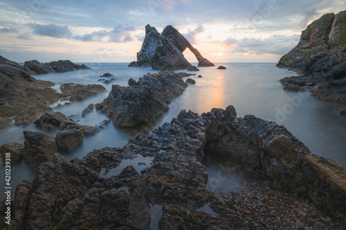 Bild auf Leinwand Beautiful dramatic sescape scenery at sunrise or sunset of Bow Fiddle Rock sea arch on the rocky shore of Portknockie on the Moray Firth in Scotland