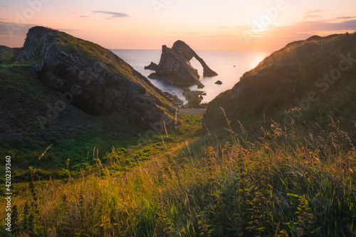 Sunrise or sunset golden light across a beatuful seascape of Bow Fiddle Rock sea arch on the rocky shore of Portknockie on the Moray Firth in Scotland. photo
