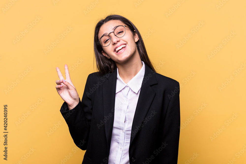 Young Indian business woman isolated on yellow background joyful and carefree showing a peace symbol with fingers. Young Indian business woman isolated on yellow background joyful and carefree showing a peace symbol with fingers.