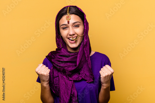 Young Indian woman wearing a traditional sari clothes isolated on yellow background cheering carefree and excited. Victory concept.