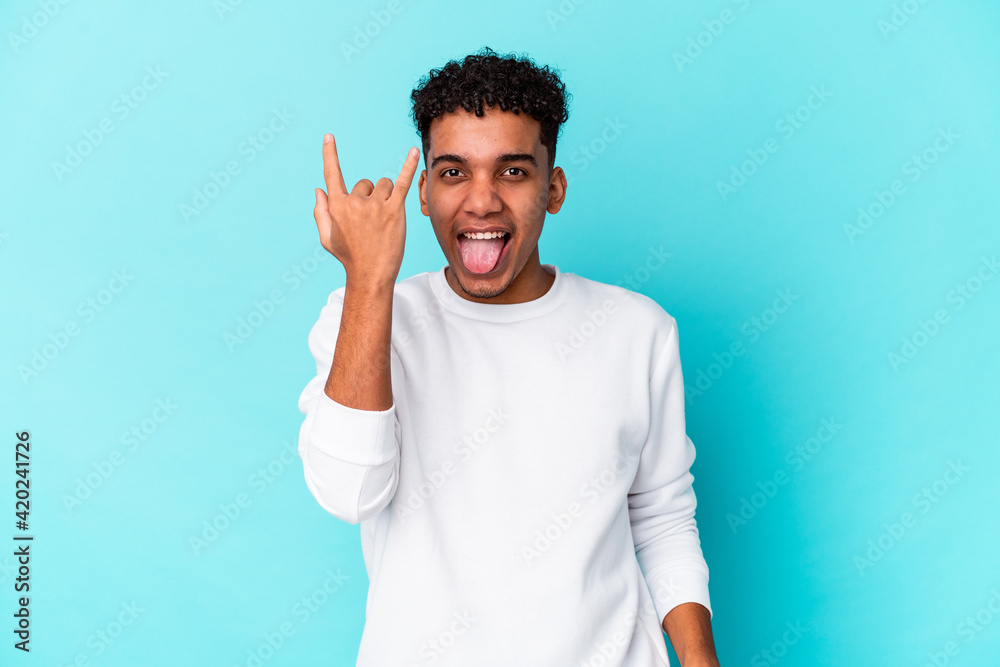 Young african american curly man isolated on blue showing rock gesture with fingers