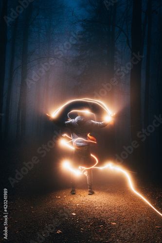 mystique in the autumn forest, where a boy in a blue jacket flies light from his left hand to his right and around his whole body. Mysterious siuleta in the wild surrounded by many lights photo