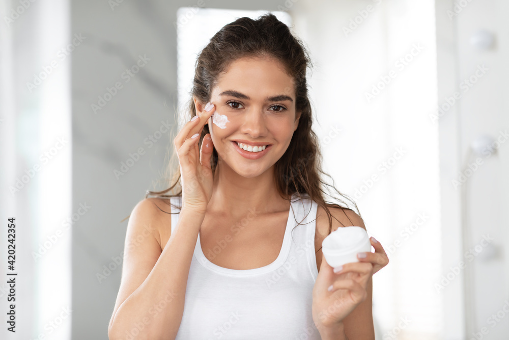 Attractive Young Woman Applying Face Cream Standing In Bathroom Indoor Attractive Young Woman Applying Face Cream Standing In Bathroom Indoor