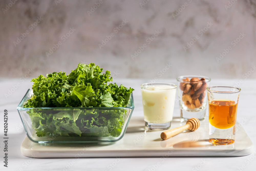 Kale in a glass bowl with greek yogurt, almond ann honey in glass on white table background for healthy smoothie. Kale is considered a superfood because it's a great source of vitamins and minerals.