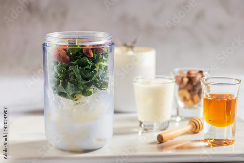 Healthy green kale smoothie in portable blender mixed greek yogurt, almond and honey on white table background. Kale is considered a superfood because it's a great source of vitamins and minerals.