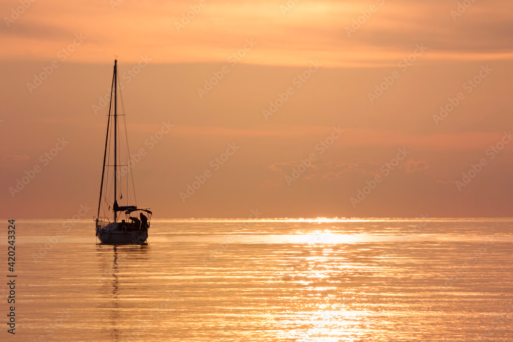 sailing boat silhouette in the distance in a calm orange glowing seamless sea.Sunset on the Adriatic Sea