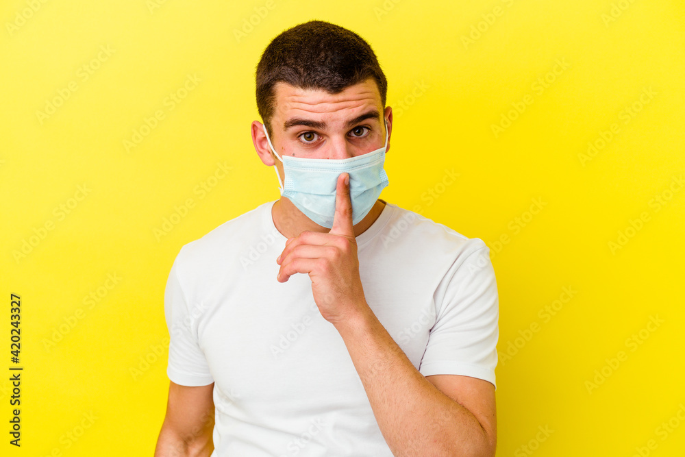 Young caucasian man wearing a protection for coronavirus isolated on yellow background keeping a secret or asking for silence. Young caucasian man wearing a protection for coronavirus isolated on yellow background keeping a secret or asking for silence.