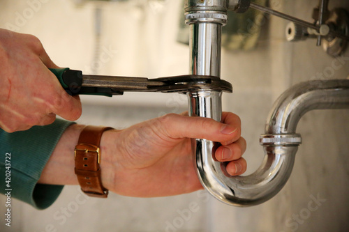 Plumber fixing sink pipe with adjustable wrench.