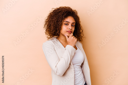 Young african american woman isolated on beige background suspicious, uncertain, examining you. © Asier