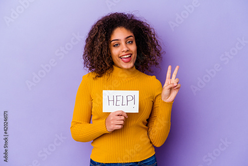 Young African American woman holding a Help placard isolated on purple background joyful and carefree showing a peace symbol with fingers. photo