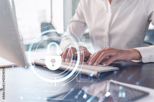 A woman programmer is typing a code on computer to protect a cyber security from hacker attacks and save clients confidential data. Padlock Hologram icons over the typing hands. Formal wear.