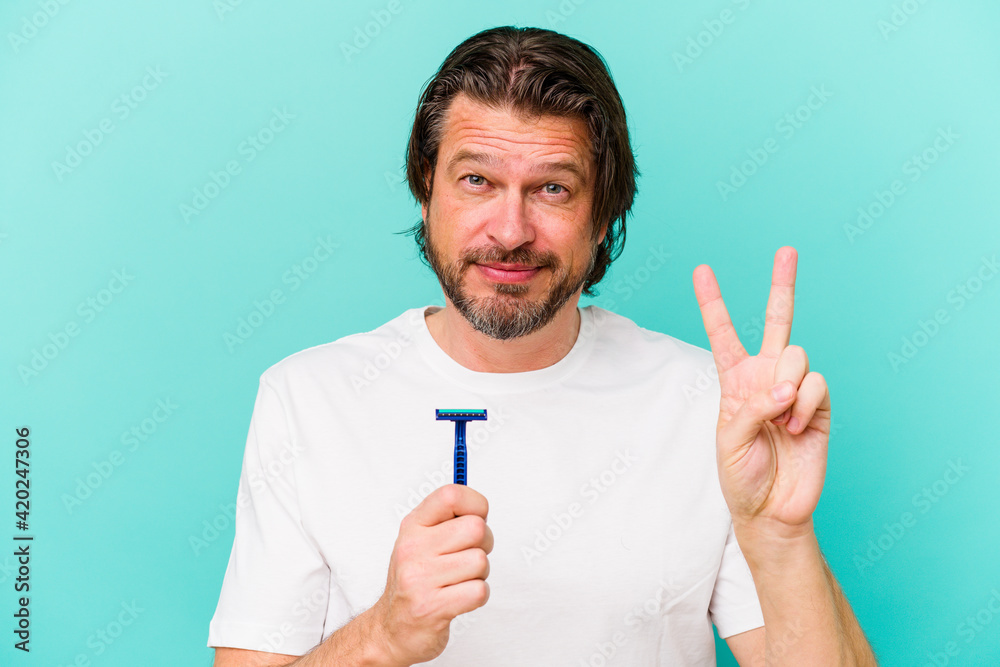 Middle age dutch man holding a razor blade isolated on blue background showing number two with fingers. Middle age dutch man holding a razor blade isolated on blue background showing number two with fingers.