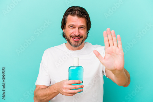 Middle age dutch man sitting holding a mouthwash isolated on blue background standing with outstretched hand showing stop sign, preventing you.
