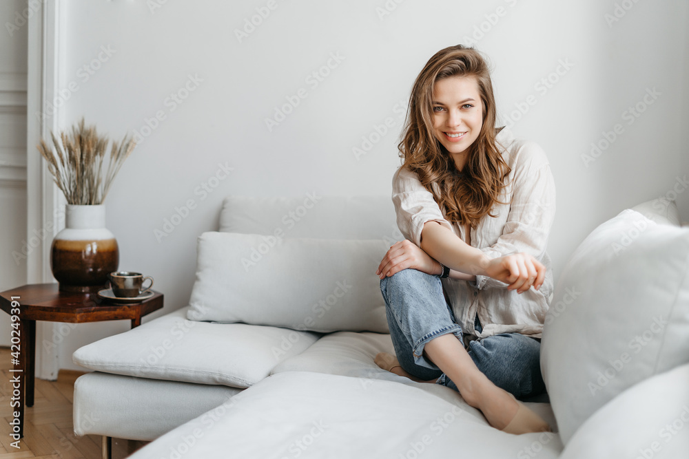 A young blonde woman in casual comfortable clothes sits on a white sofa at home A young blonde woman in casual comfortable clothes sits on a white sofa at home