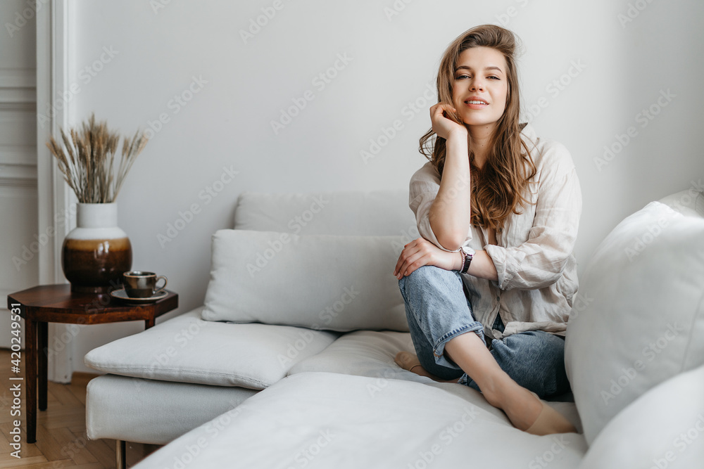 A young blonde woman in casual comfortable clothes sits on a white sofa at home A young blonde woman in casual comfortable clothes sits on a white sofa at home