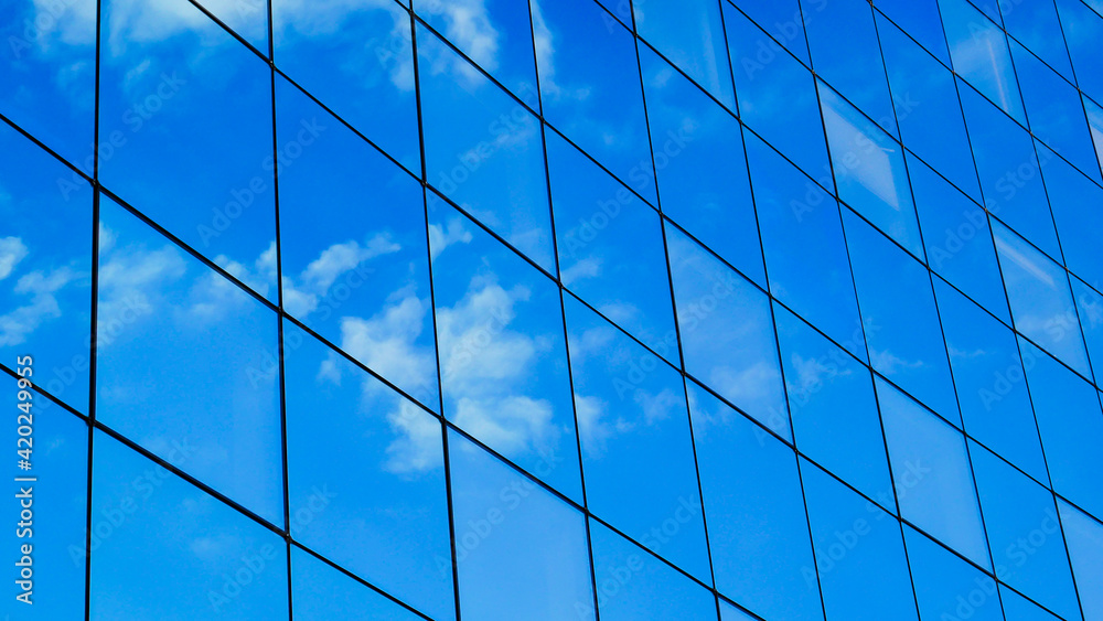 transparent glass wall of office building, sky and clouds reflecting transparent glass wall of office building, sky and clouds reflecting