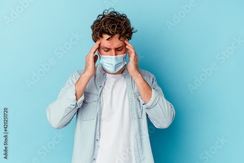 Young caucasian man wearing an antiviral mask isolated on blue background touching temples and having headache. © Asier