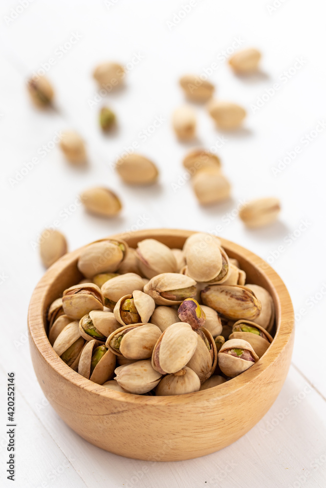Pistachio nuts in a wooden bowl on white background Pistachio nuts in a wooden bowl on white background