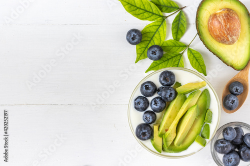 Top view of organic yogurt topped with avocado and blueberry on white wooden background, healthy and nutritious diet