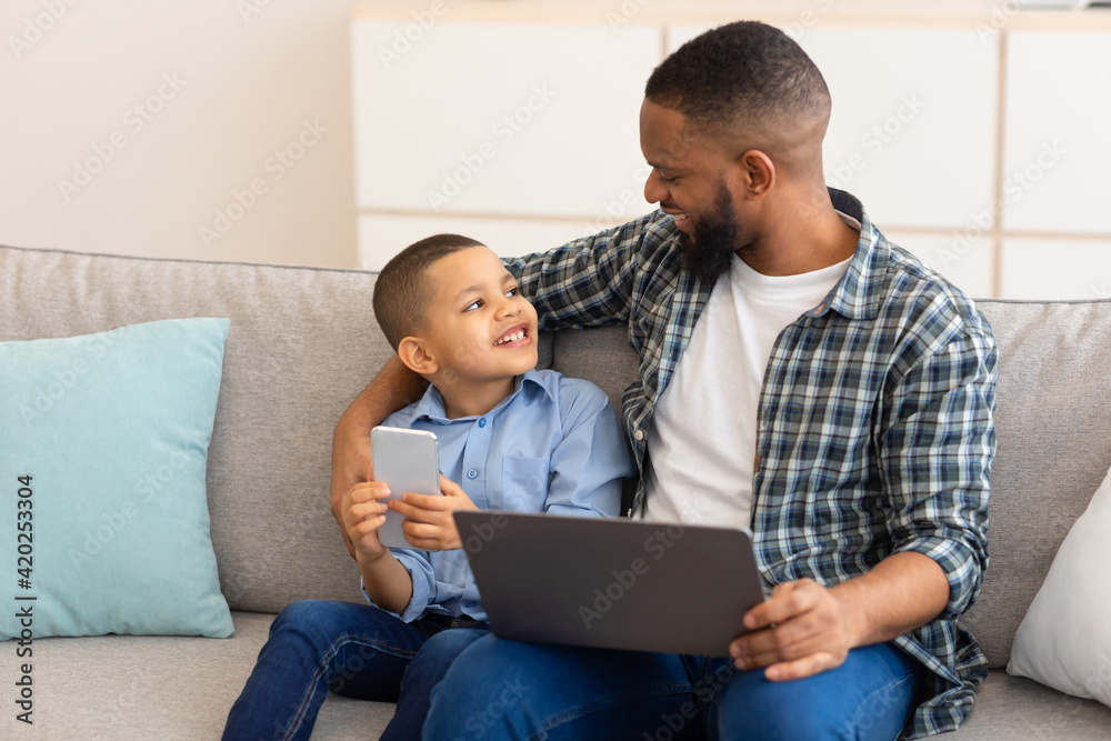 African Father And Son Using Laptop And Phone At Home African Father And Son Using Laptop And Phone At Home