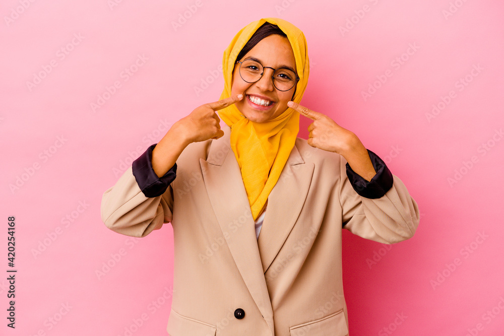 Young business muslim woman isolated on pink background smiles, pointing fingers at mouth.