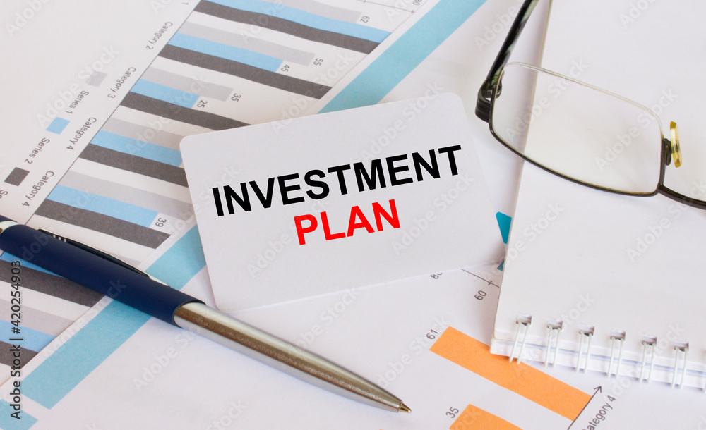 Business card with text Investment Plan lies on financial charts with pen and eyeglass Business card with text Investment Plan lies on financial charts with pen and eyeglass
