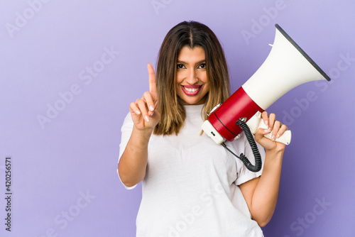 Young indian woman holding a megaphone isolated showing number one with finger.