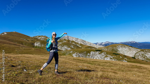 A woman with a hiking backpack hiking pointing with her finger to the peak of Hohe Weichsel in Austria. The peak is her destination. Lush green pasture around her. Exploration and discovery