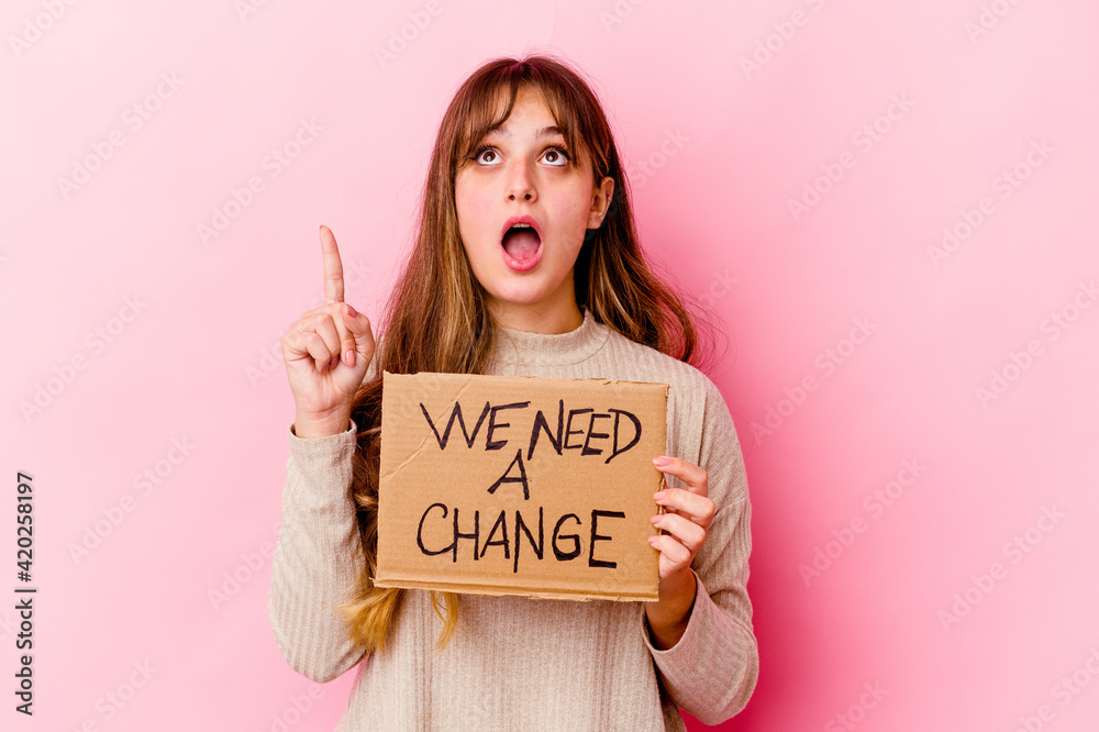 Young caucasian woman holding a We need a change placard isolated pointing upside with opened mouth. Young caucasian woman holding a We need a change placard isolated pointing upside with opened mouth.
