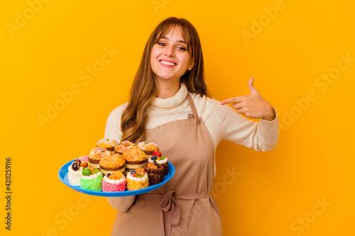 Young pastry chef woman isolated on yellow background person pointing by hand to a shirt copy space, proud and confident