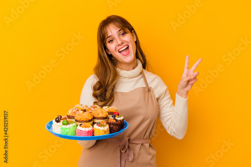 Young pastry chef woman isolated on yellow background joyful and carefree showing a peace symbol with fingers.