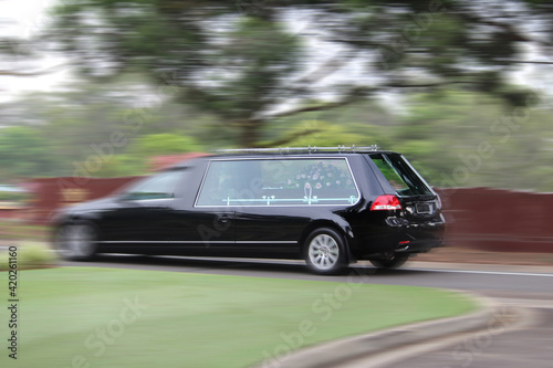 A generic black hearse with a coffin driving through a cemetery. Motion blur photo