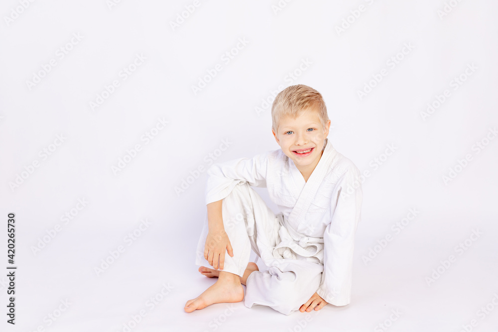judo and sports concept, blond boy sitting in kimono on white background, place for text judo and sports concept, blond boy sitting in kimono on white background, place for text