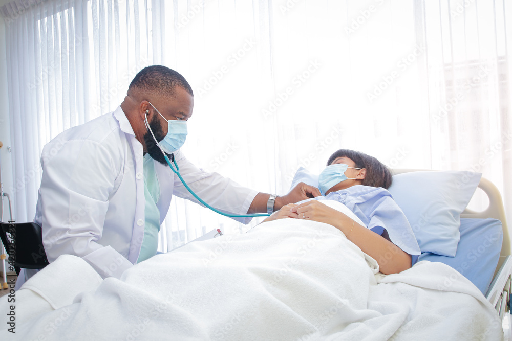African American male doctor Check the illness of a woman lying in a hospital bed. Treatment of patients during the coronavirus epidemic. Concept of medical service. African American male doctor Check the illness of a woman lying in a hospital bed. Treatment of patients during the coronavirus epidemic. Concept of medical service.