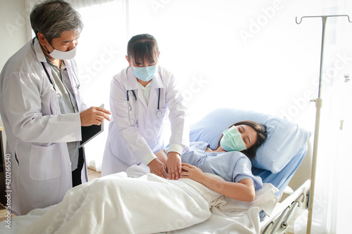 Two Asian doctors examined the abdominal pain of a woman lying in a hospital bed. Treatment of patients during the coronavirus epidemic. Concept of medical service