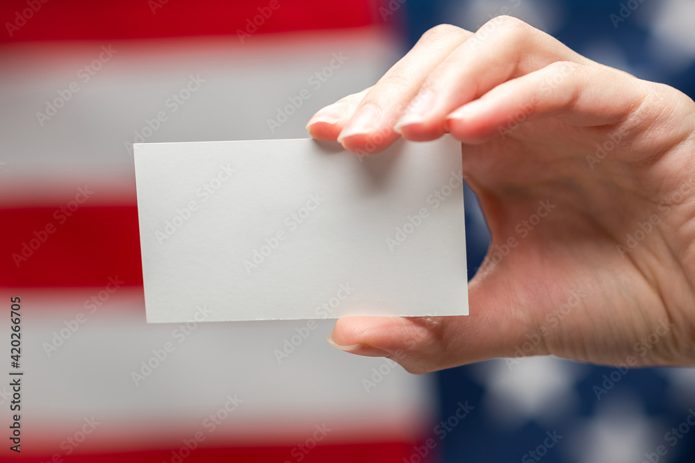 Empty card in woman hand. Copy space. American flag background. Empty card in woman hand. Copy space. American flag background.