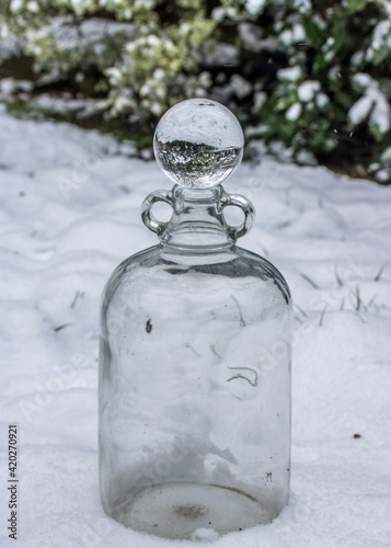snowy garden scene reflected in a crystal ball balanced on top of a demijohn