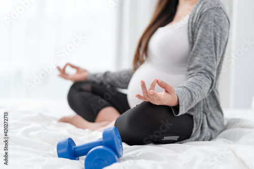 Asian happy pregnant woman is sitting and exercise on the bed. pregnancy, motherhood, people and expectation concept