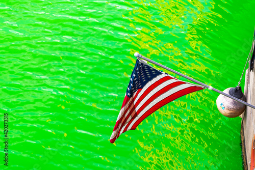 Konstfotografi An American flag hangs down next to a life ring and buoy above the freshly dyed bright green river in downtown Chicago in 2021 making a great St