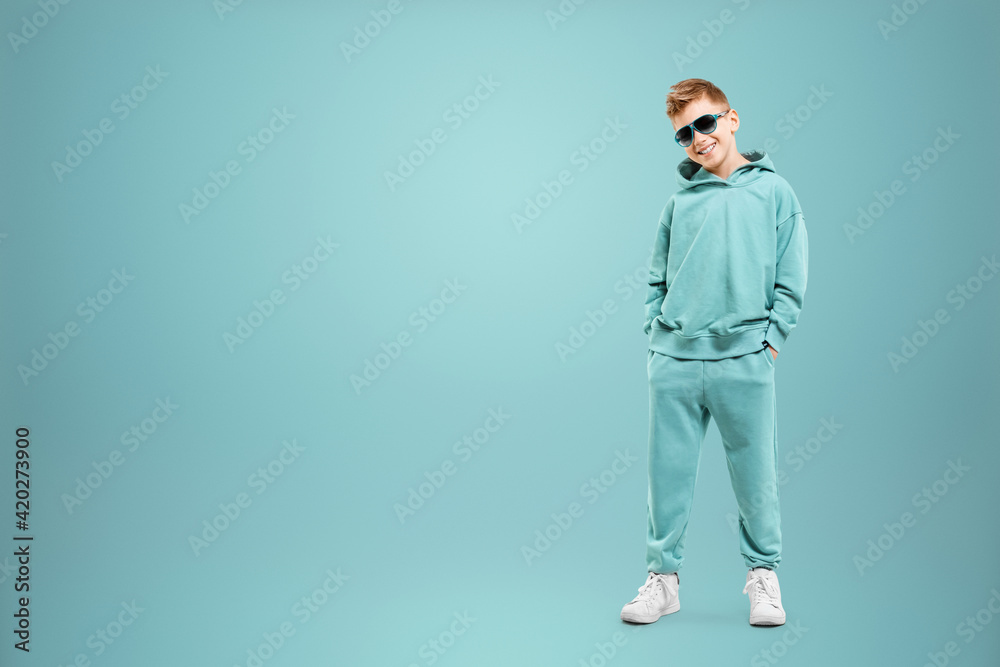 Fototapeta premium Little in a turquoise suit poses and fools around on a turquoise background, looks at the camera. Children's studio portrait. Childhood lifestyle concept.