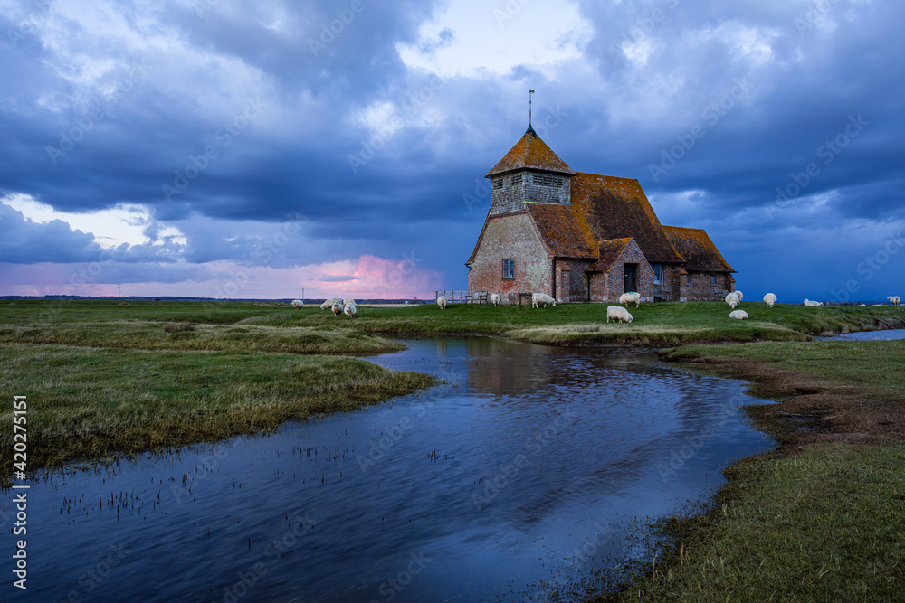 Saint Thomas Church near Fairfield on the Romney Marsh in Kent south east England, storm clouds gathering during blue hour and sheep grazing