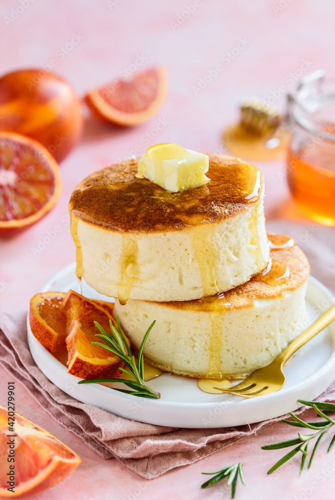 Fluffy Japanese Soufflé pancakes with honey and red oranges on a white plate. Asian food. Pink background. Selective focus Fluffy Japanese Soufflé pancakes with honey and red oranges on a white plate. Asian food. Pink background. Selective focus